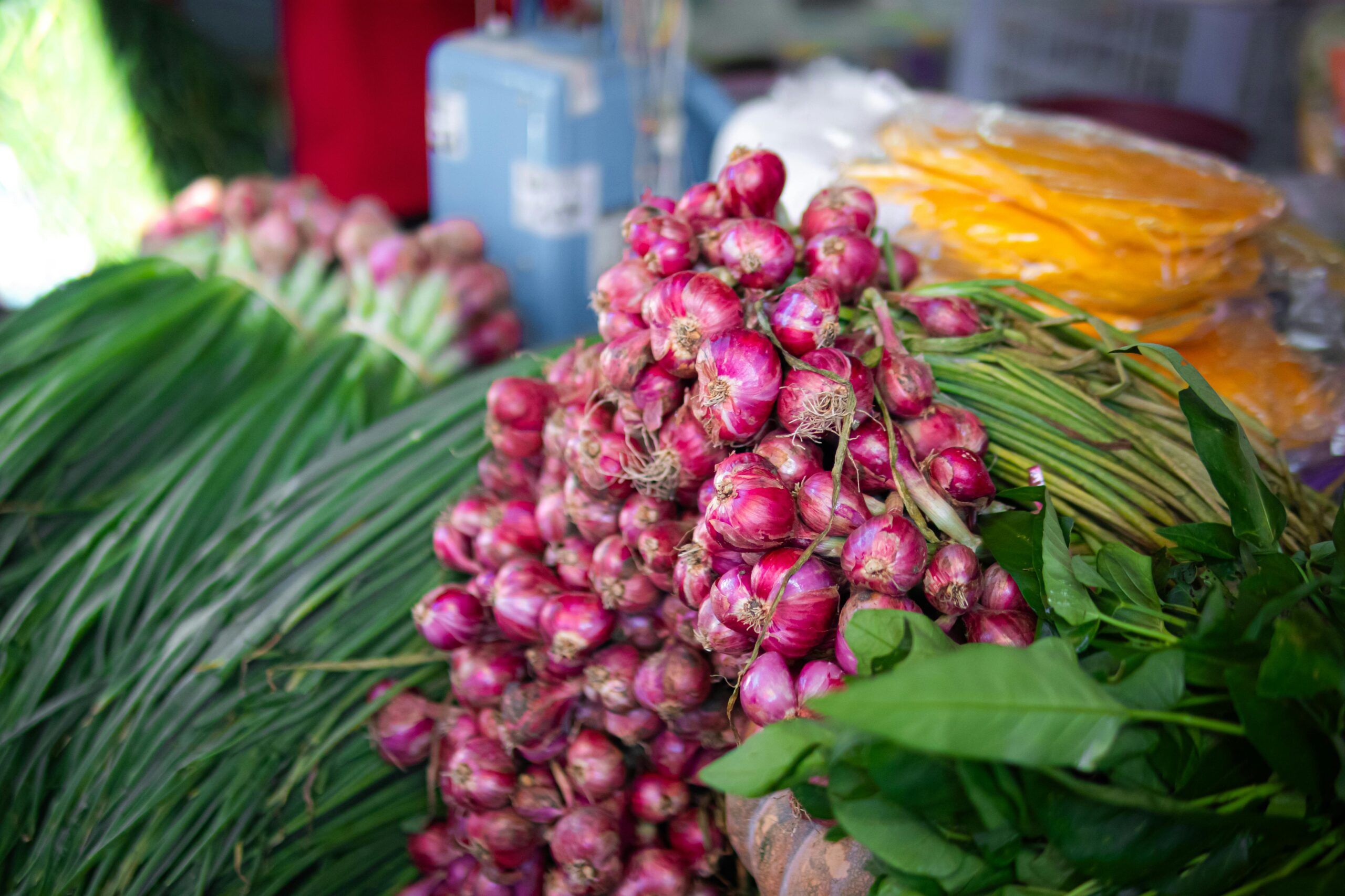 A vibrant display of fresh red onions and greens at a bustling market stall.